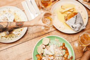 Milieu de table représentant un bon repas avec ambiance festive d'une main qui attrape un verre d'alcool