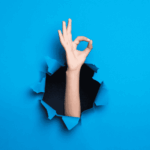 Bras traversant une paroi bleue avec un geste « OK », illustrant la facilité d’utilisation et la manipulation quotidienne d’une aide auditive.