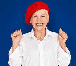 Femme âgée souriante portant un béret rouge, symbole d’une approche personnalisée du choix d’une aide auditive.