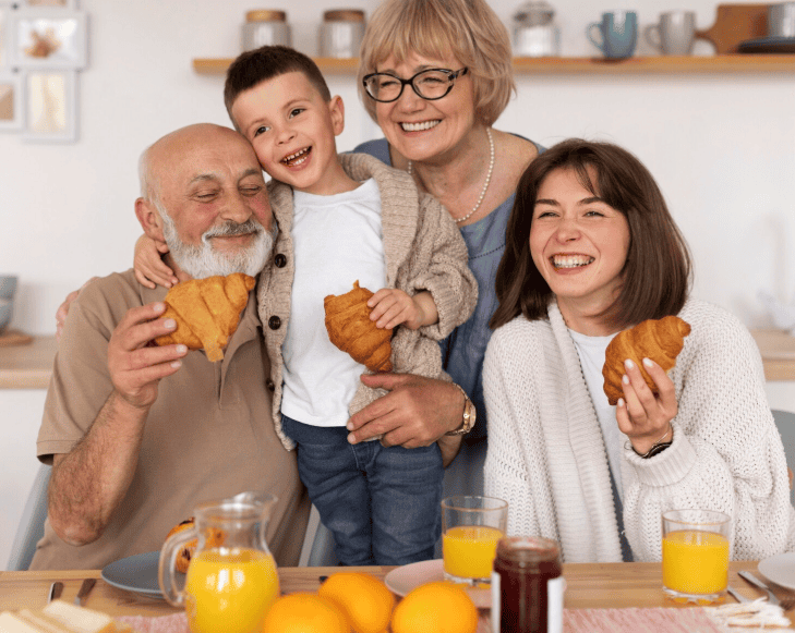 Grands-parents, fille et petit-fils souriants partageant un moment convivial autour de croissants.