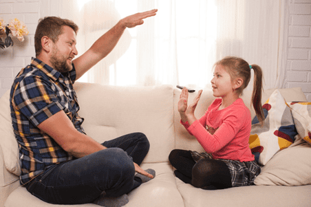 Père discutant et jouant avec sa fille sur un canapé à la maison.