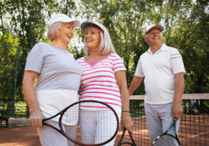 Trois personnes âgées jouent au tennis, raquette à la main, sur un court.